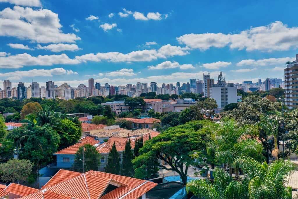 Vista panorâmica da cidade com edifícios e vegetação ao fundo.