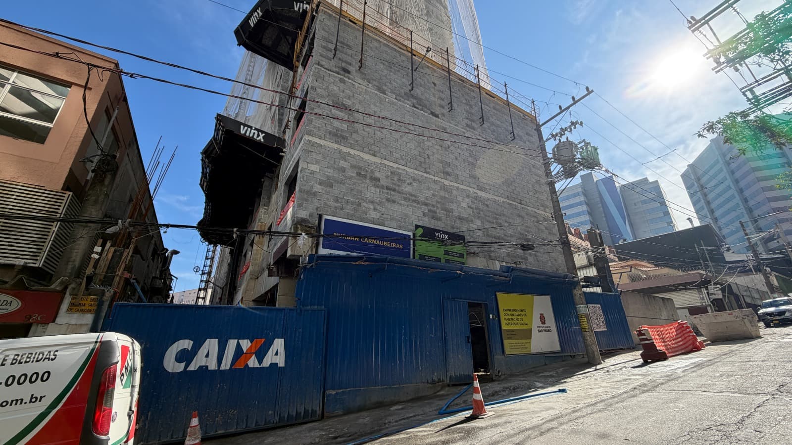 Edifício em fase inicial de obras com tapumes azuis e estrutura de blocos.