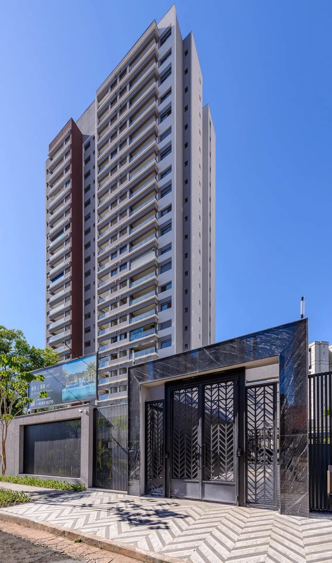 Fachada do edifício residencial com portão de entrada e calçada decorada.