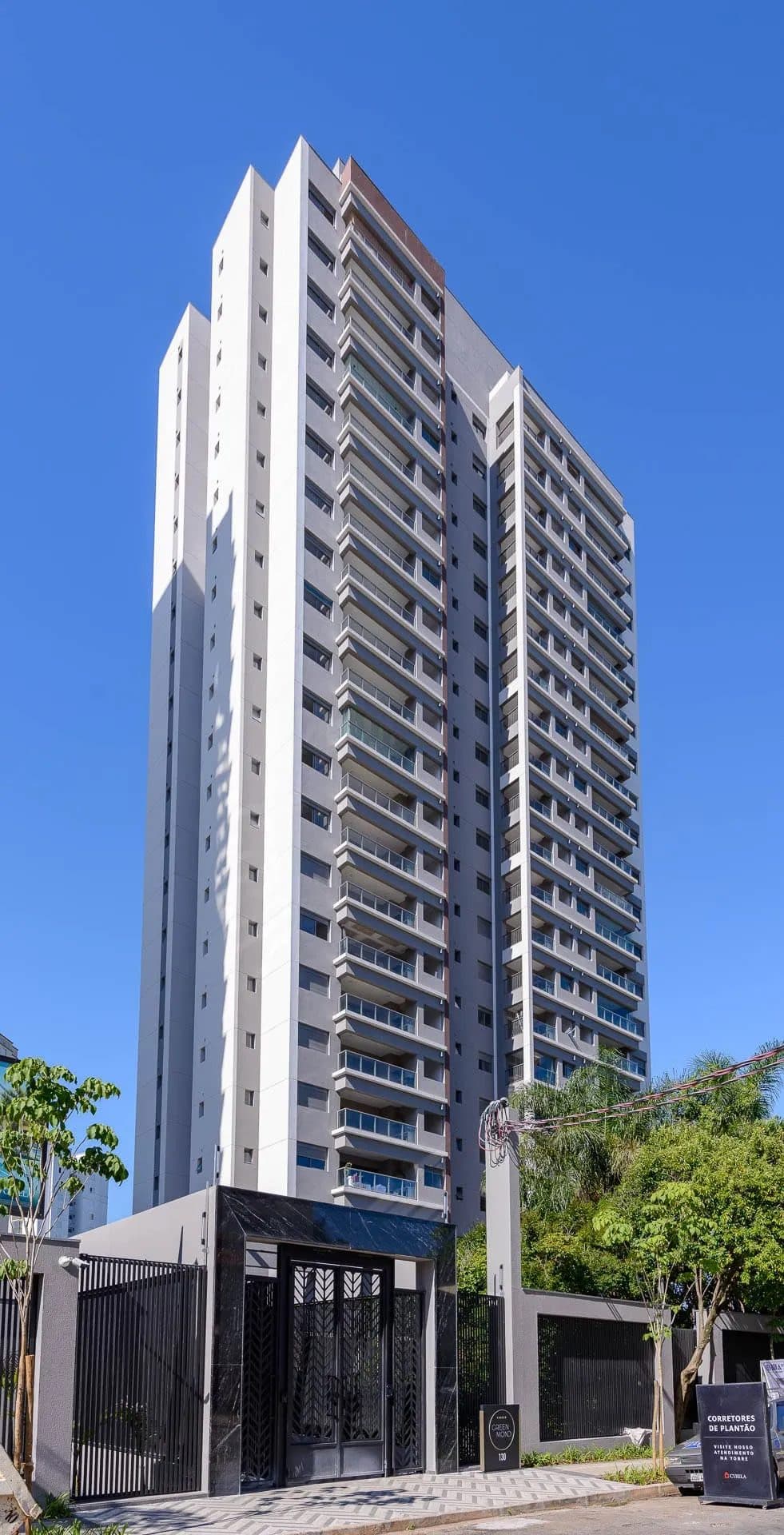 Vista externa da torre residencial com varandas e portaria ao fundo.