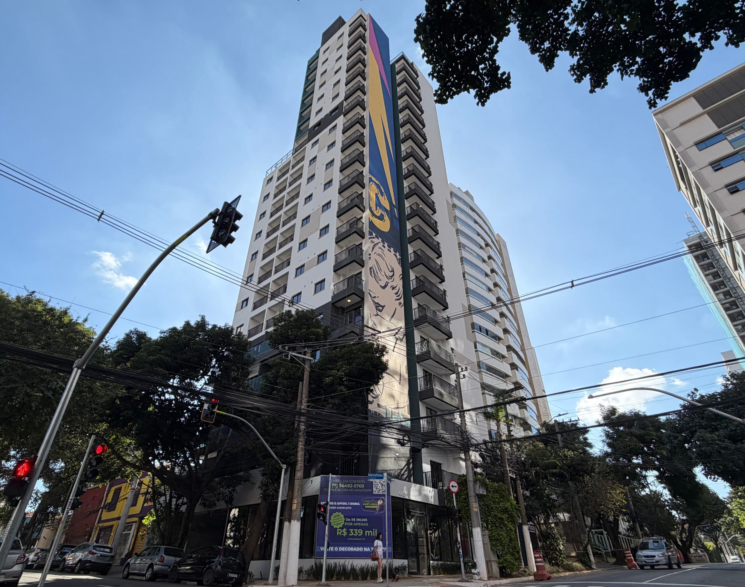 Vista externa da fachada do edifício residencial com pintura lateral e rua em primeiro plano.