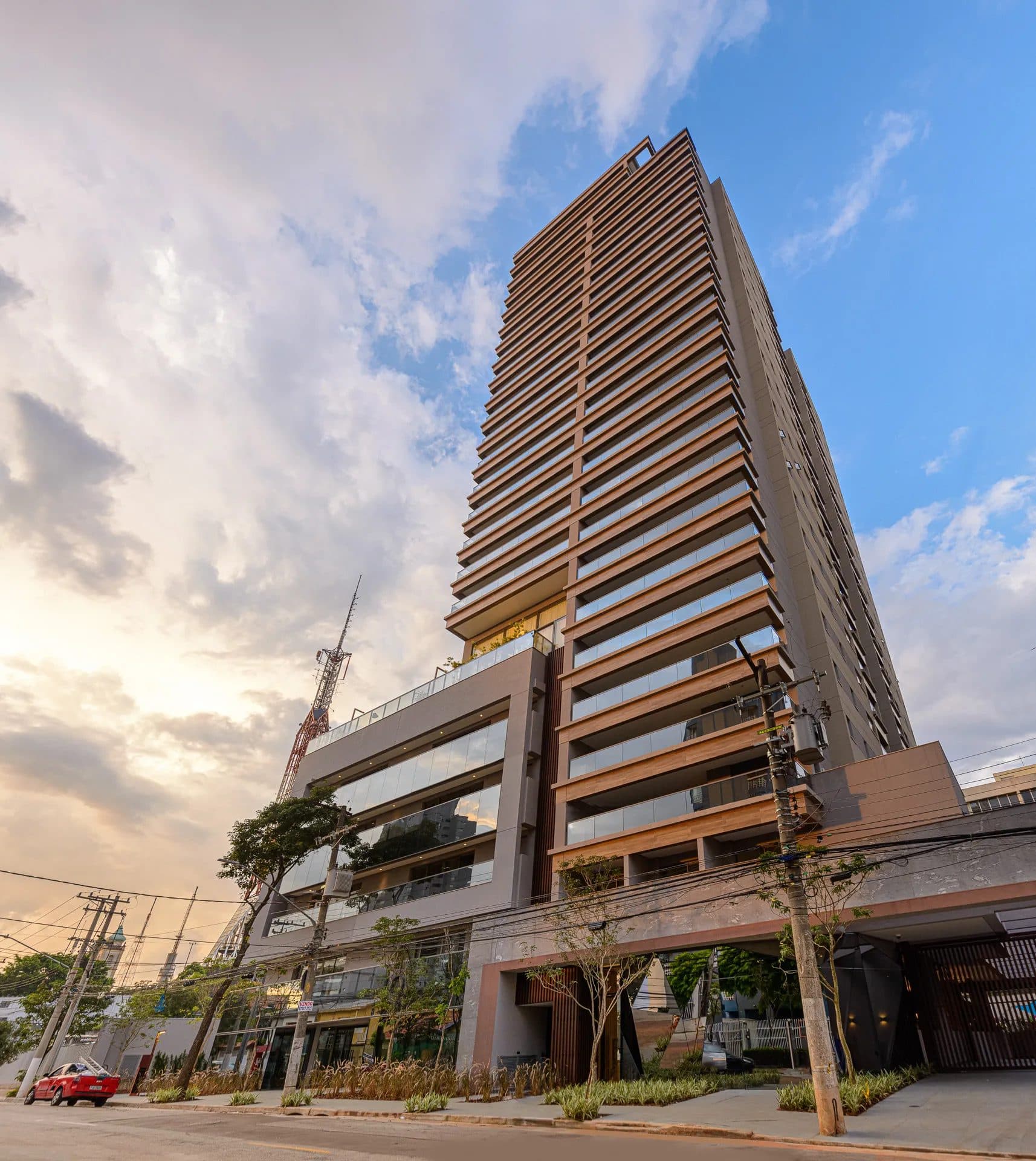 Fachada externa do edifício residencial com varandas e estrutura em tons terrosos e cinza.
