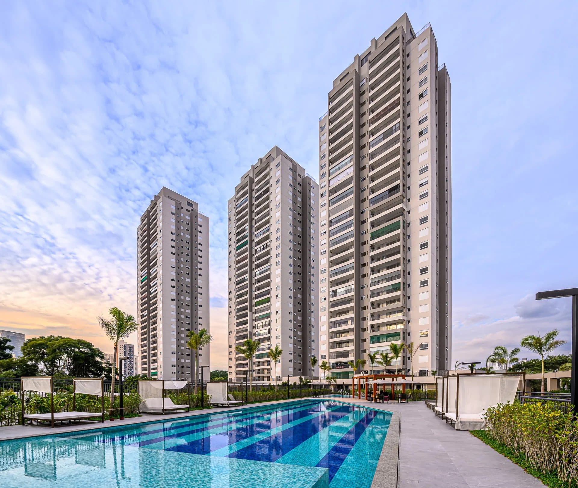 Fachada externa das torres residenciais com piscina em primeiro plano e espreguiçadeiras.