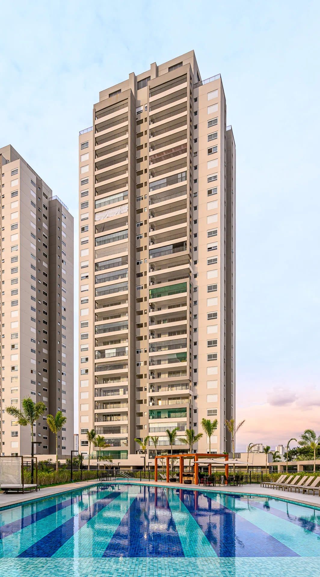 Vista vertical da fachada de torre residencial com varandas e piscina na área externa.