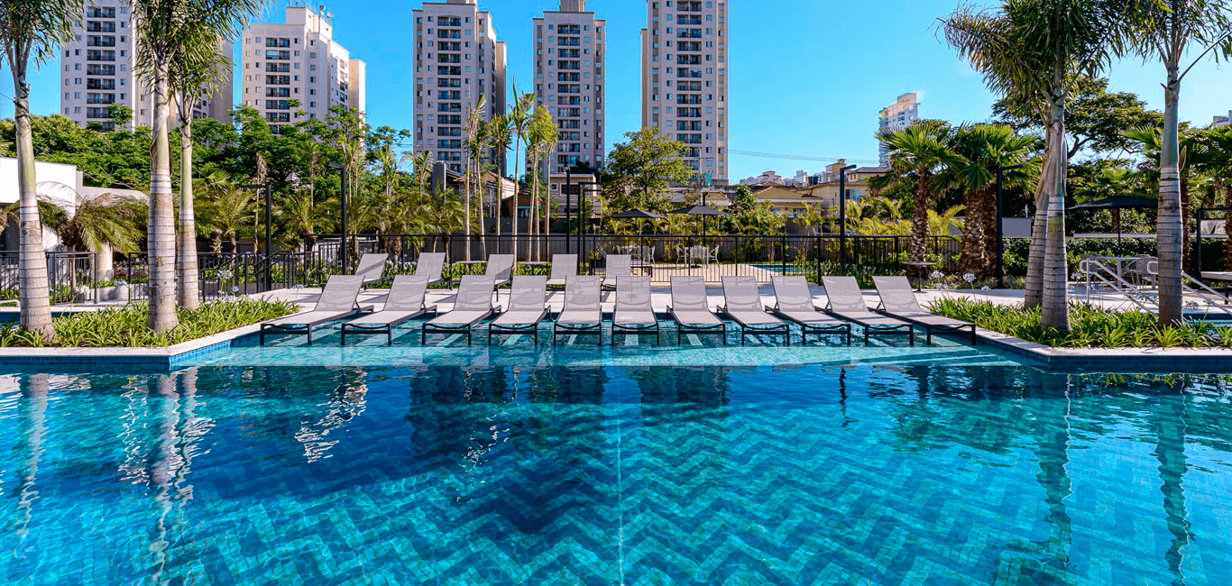 Piscina externa com espreguiçadeiras e edifícios ao fundo